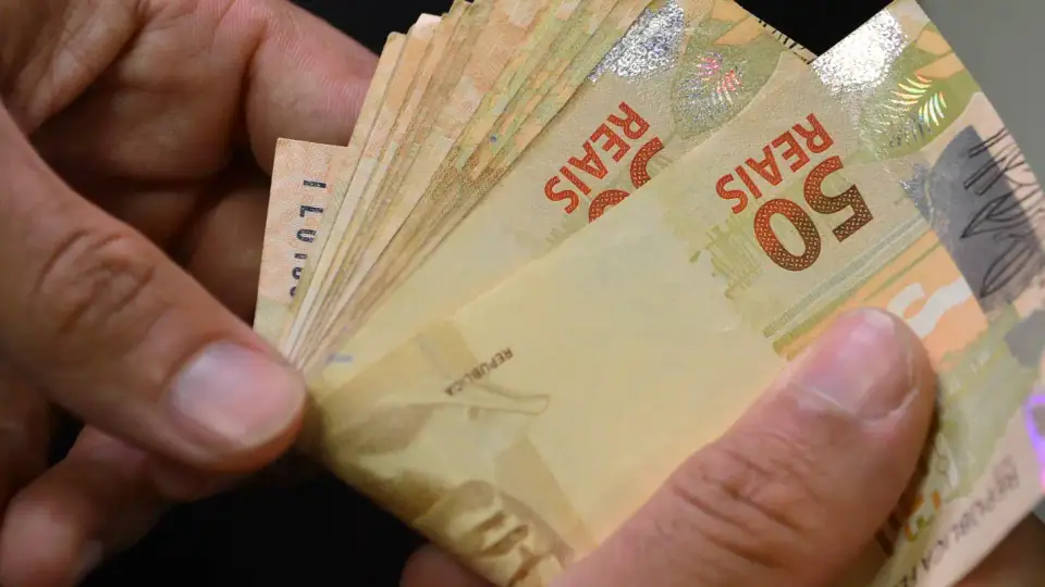 Cédulas e moedas de real espalhadas sobre uma superfície