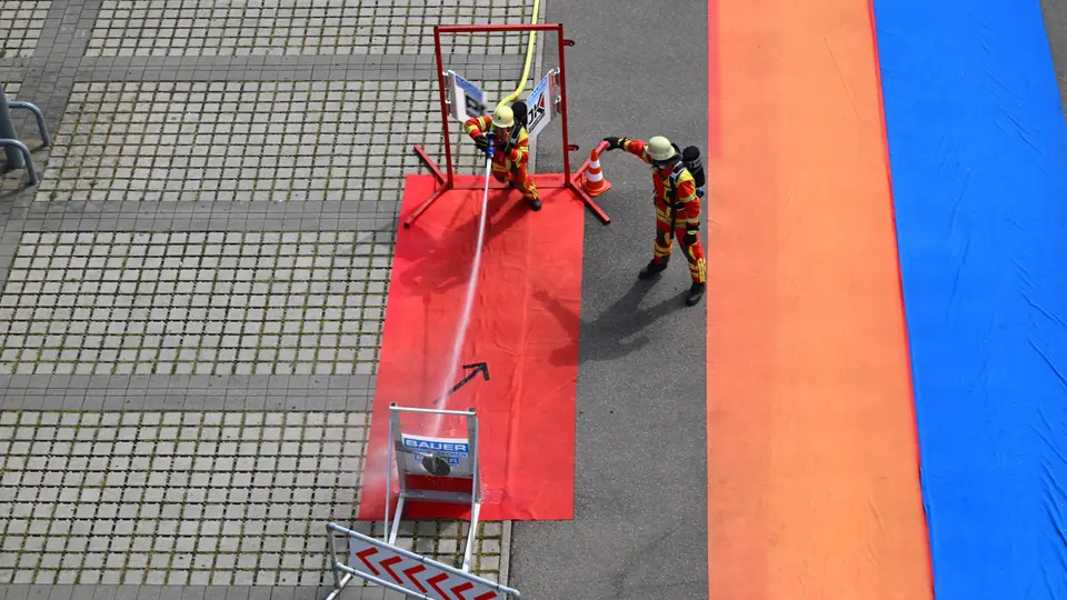 Equipe de bombeiros em treinamento com mangueira em instalação externa