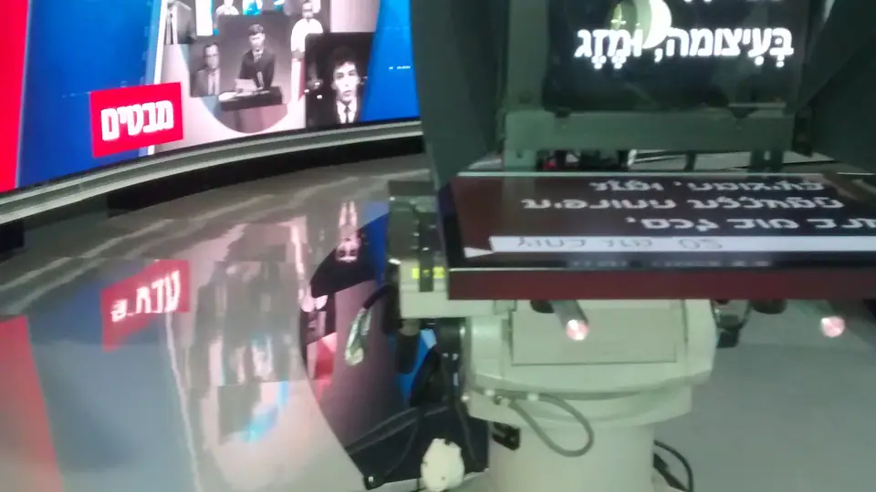 Estúdio de telejornal israelense com bancada e luzes de estúdio